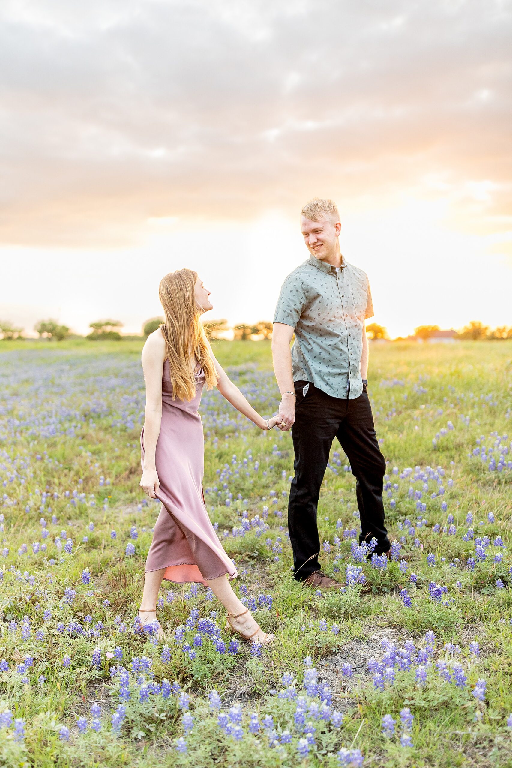 engaged couple walk through field of bluebonnets in Brenham, TX