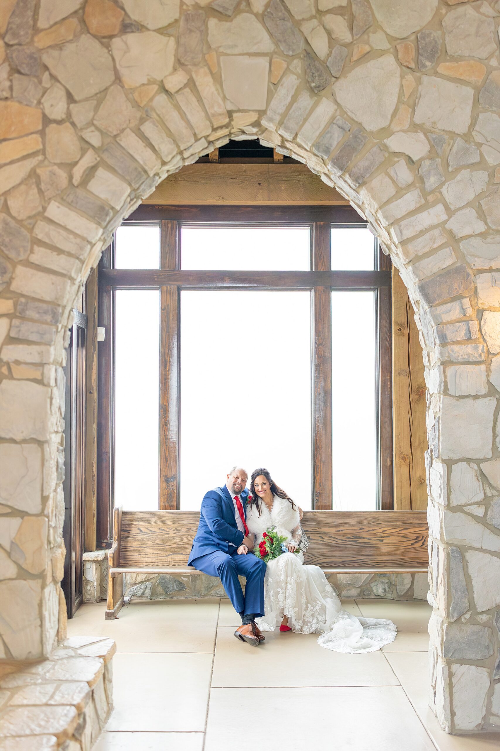 bride and groom sit on bench inside chapel 